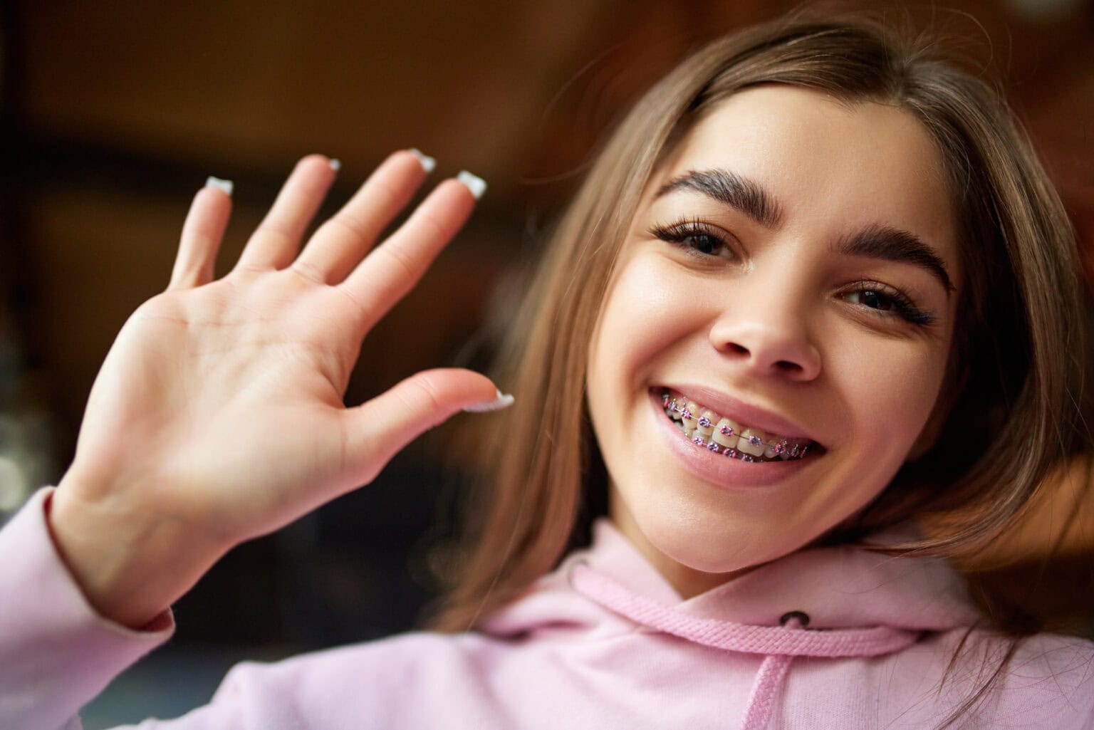 Girl in a pink hoodie smiling with braces